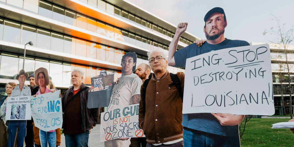 Levensgroot uit hout gesneden portretten van activisten staan voor het ING-hoofdkantoor. Op de voorgrond het portret van James Hiatt. Hij houdt een bord vast met de tekst: 'ING stop destroying Louisiana'.