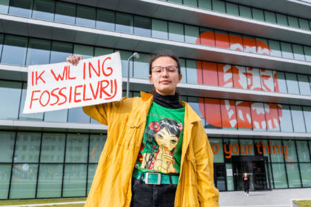 Voor het ING-hoofdkantoor houdt iemand een bordje vast met de tekst "ING Fossielvrij"