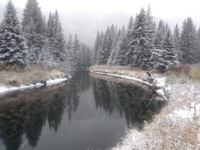 Bevroren rivier met besneeuwde bomen eromheen.